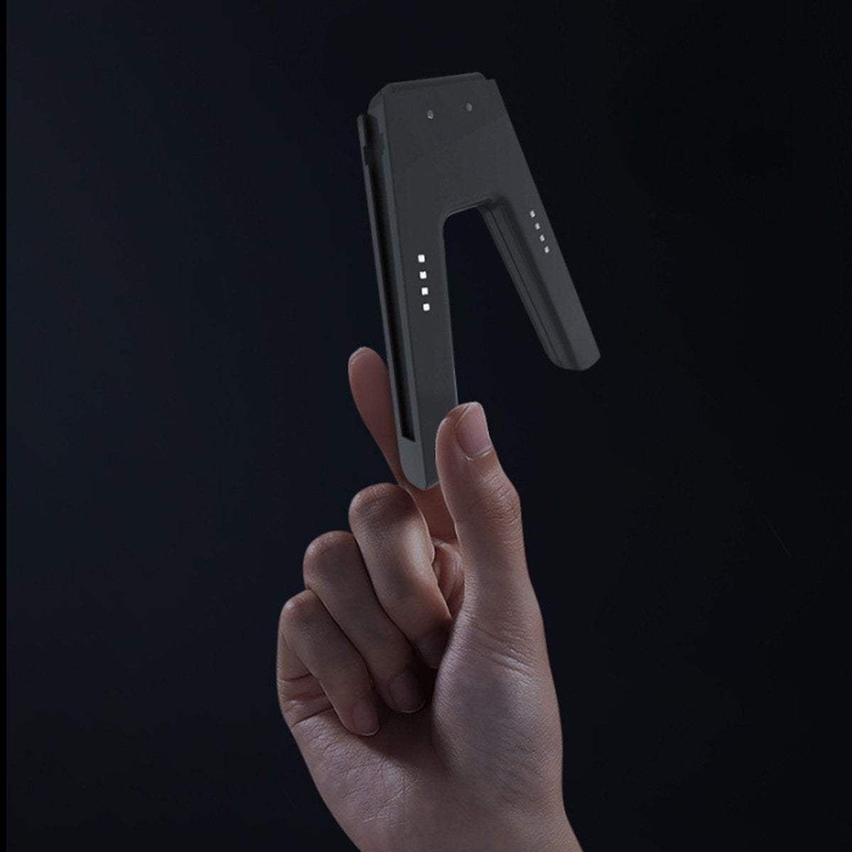 Hand holding a small electronic device against a black background