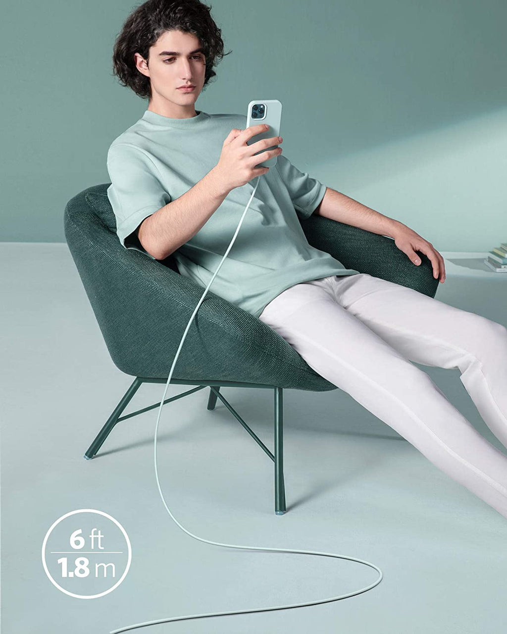 Person sitting in a chair holding a phone with a long cable, on a light gray background.