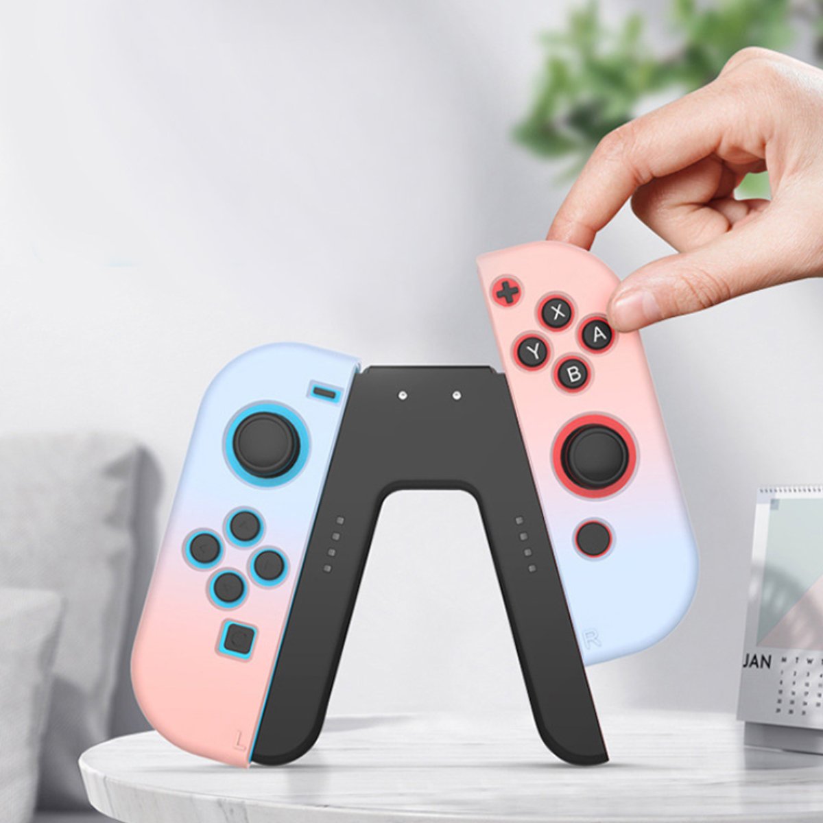 Two gaming controllers, one pink and one blue, on a white surface with a hand holding the pink controller.