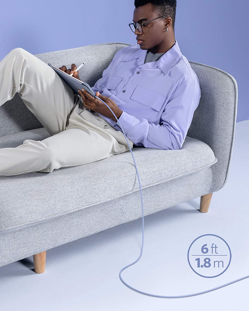 Person sitting on a gray couch using a tablet with a cable, against a light blue background.