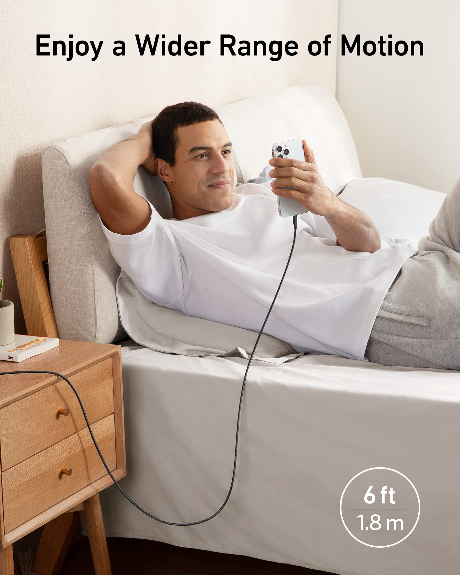 Man lying on a bed using a smartphone with a long cable, text 'Enjoy a Wider Range of Motion' and '6 ft 18 m' displayed.