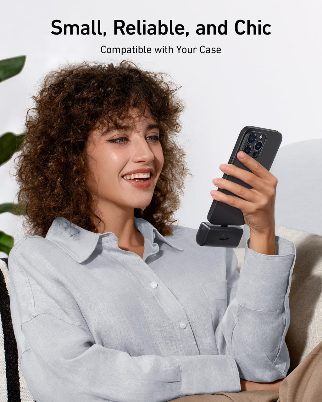 Woman holding a phone with a case, sitting on a couch with a neutral background