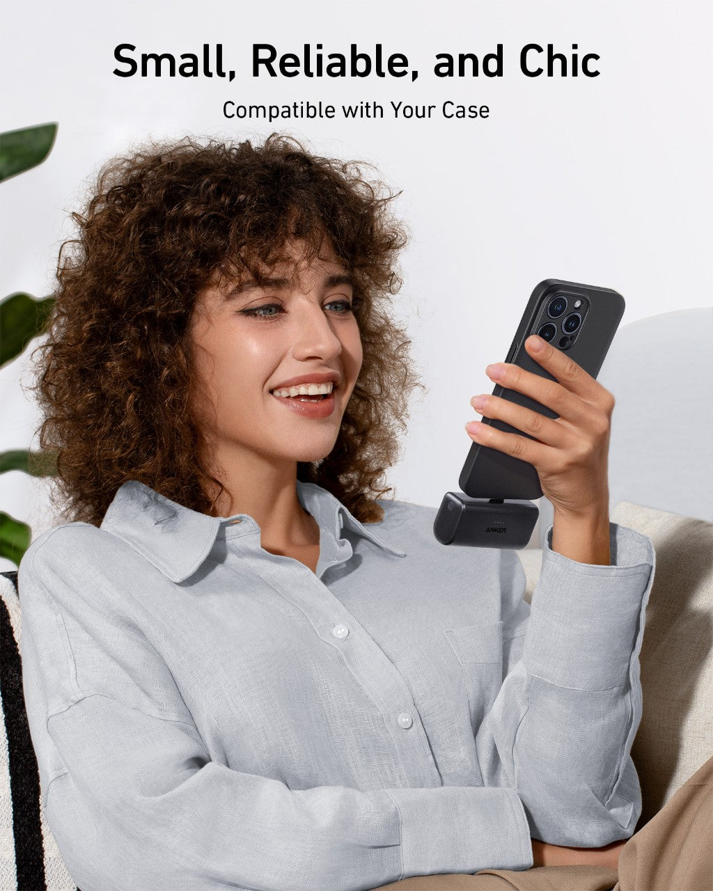Woman holding a phone with a case, sitting on a couch with a neutral background