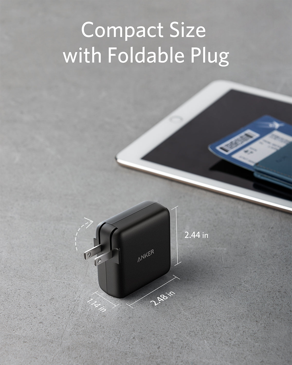 Compact Anker charger with foldable plug on a gray surface, next to a tablet.