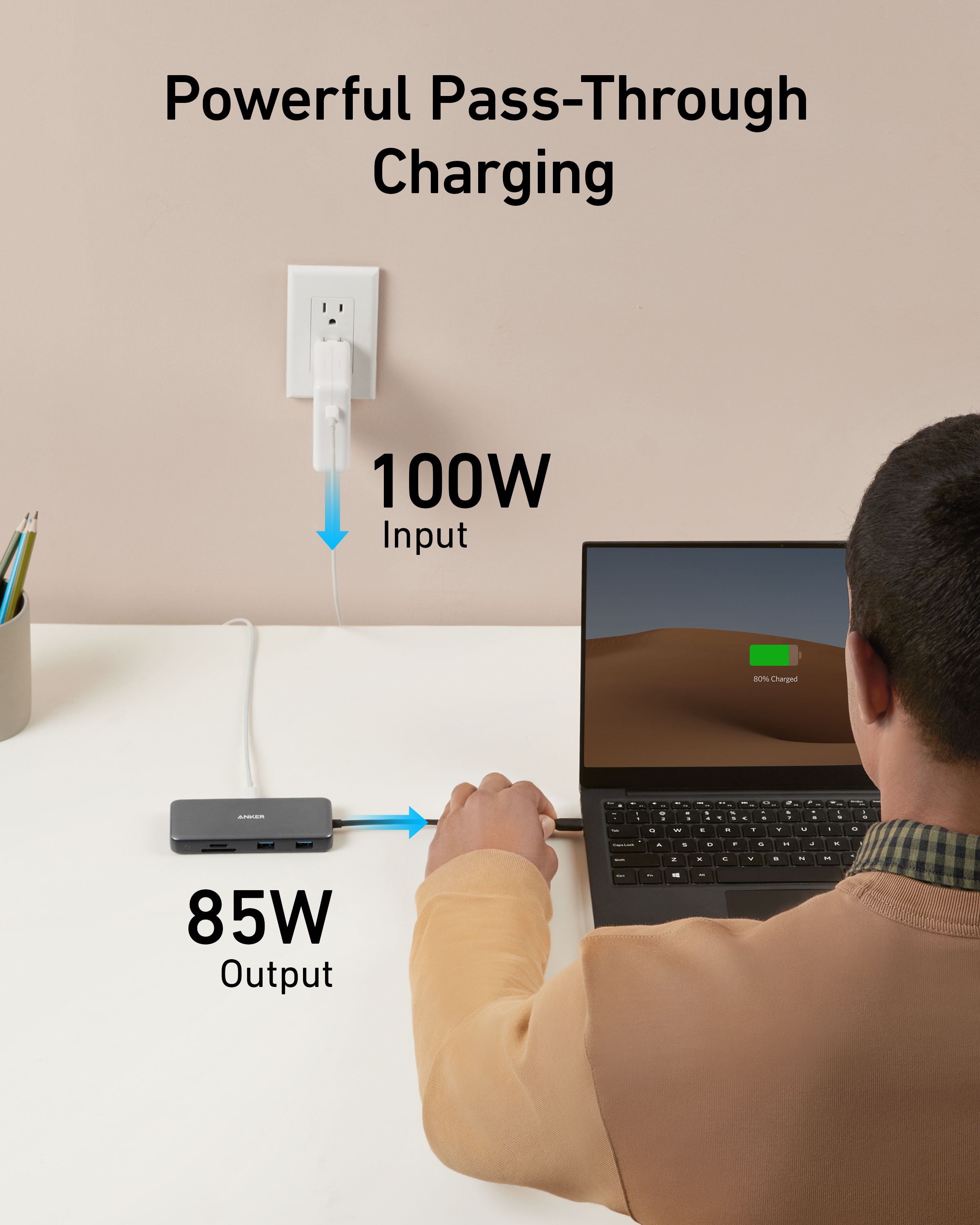Person using a laptop with a power adapter, showing 100W input and 85W output, on a desk.