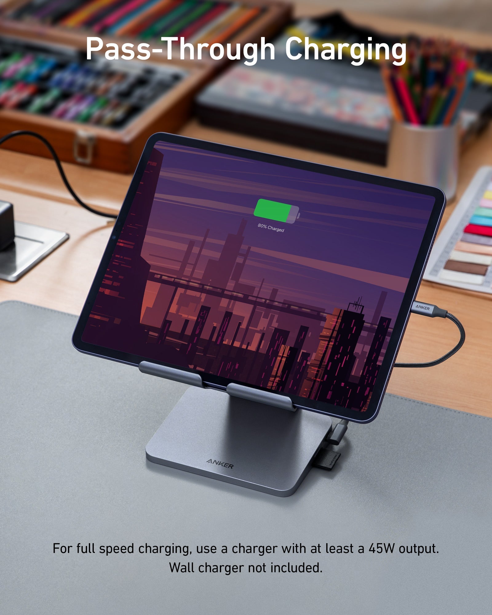 Tablet on a stand with pass-through charging feature on a desk with stationery items.