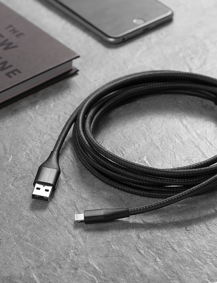Black USB cable on a gray surface with a phone and book in the background