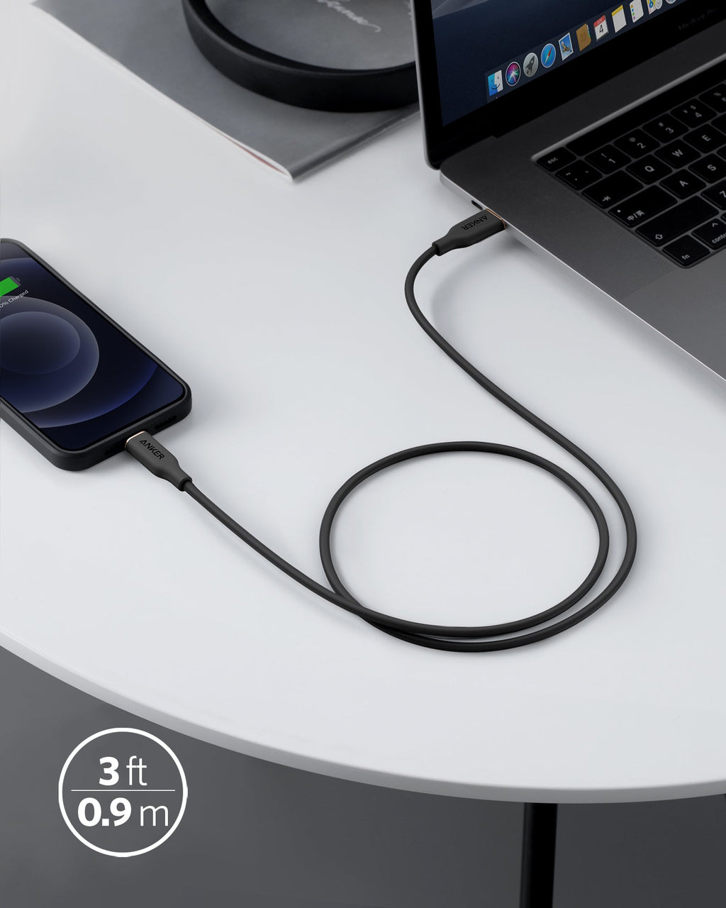 Black cable connecting a smartphone to a laptop on a white surface.