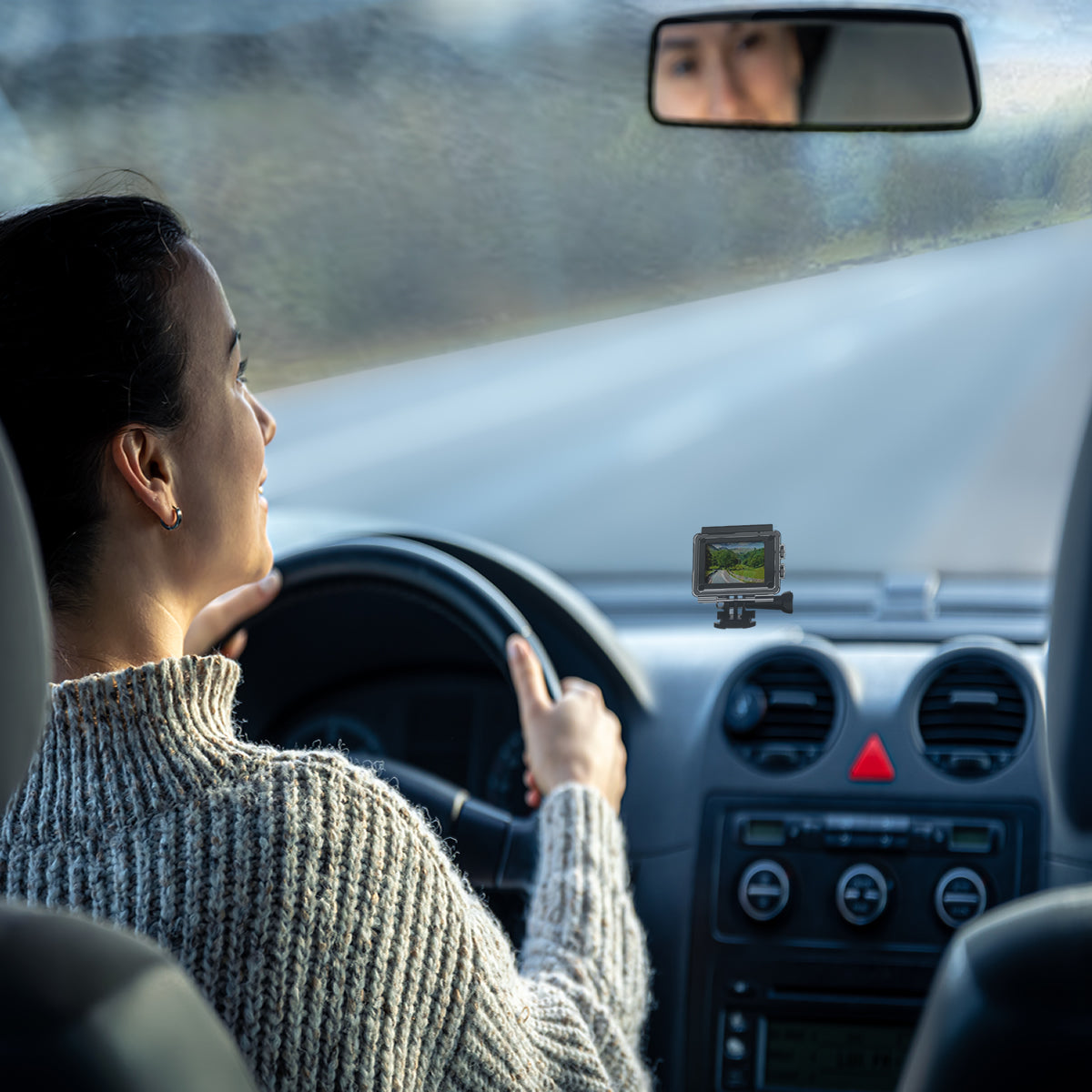 Woman driving a car with a small screen device on the dashboard.
