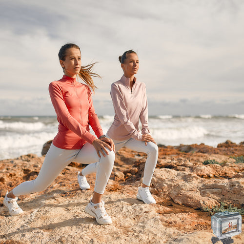 Two women exercising on rocky terrain by the ocean with a product box in the corner.
