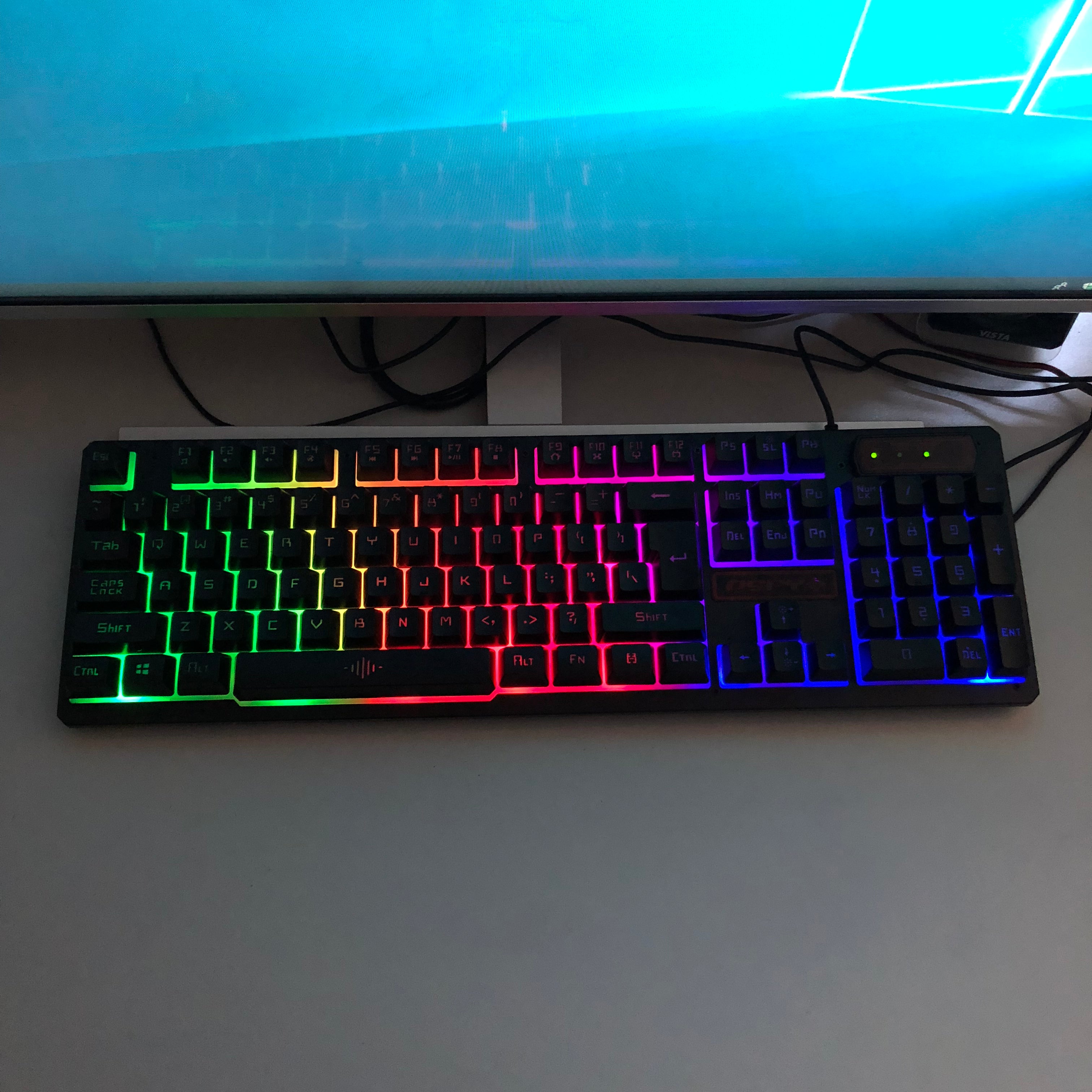 Gaming keyboard with RGB lighting in front of a computer monitor on a desk.
